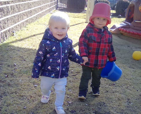 Young little boys holding each others hands one holding a plastic bucket with a bucket on his head at a Preschool & Daycare/Childcare Center serving Apex & Fuquay-Varina, NC