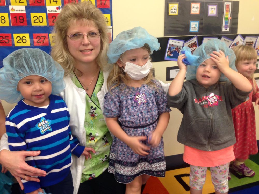 Little young kids wearing protective mask and hair net with teacher at a Preschool & Daycare/Childcare Center serving Apex & Fuquay-Varina, NC