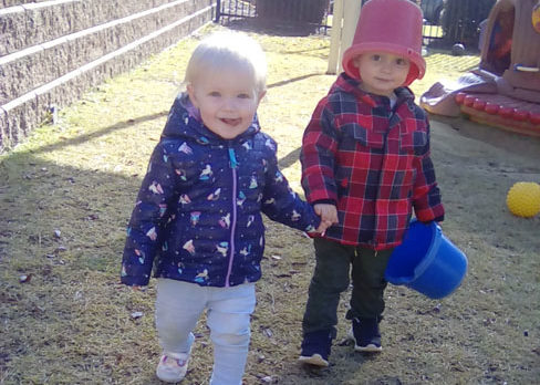 Young little boys holding each others hands one holding a plastic bucket with a bucket on his head at a Preschool & Daycare/Childcare Center serving Apex & Fuquay-Varina, NC