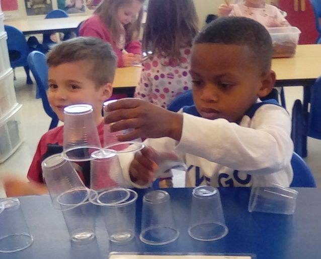 Young little kid boys playing with empty plastic cups making a pyramid cups at a Preschool & Daycare/Childcare Center serving Apex & Fuquay-Varina, NC