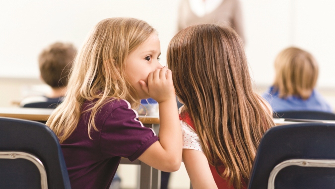 Young little girl whispering on the ear of another preschool girl at a Preschool & Daycare/Childcare Center serving Apex & Fuquay-Varina, NC