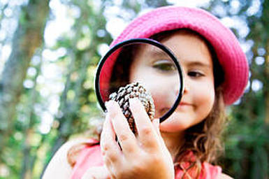 Young little preschool girl using a magnifying glass trying to check a shell at a Preschool & Daycare/Childcare Center serving Apex & Fuquay-Varina, NC