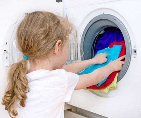 Young little girl putting some laundry in a washing machine at a Preschool & Daycare/Childcare Center serving Apex & Fuquay-Varina, NC