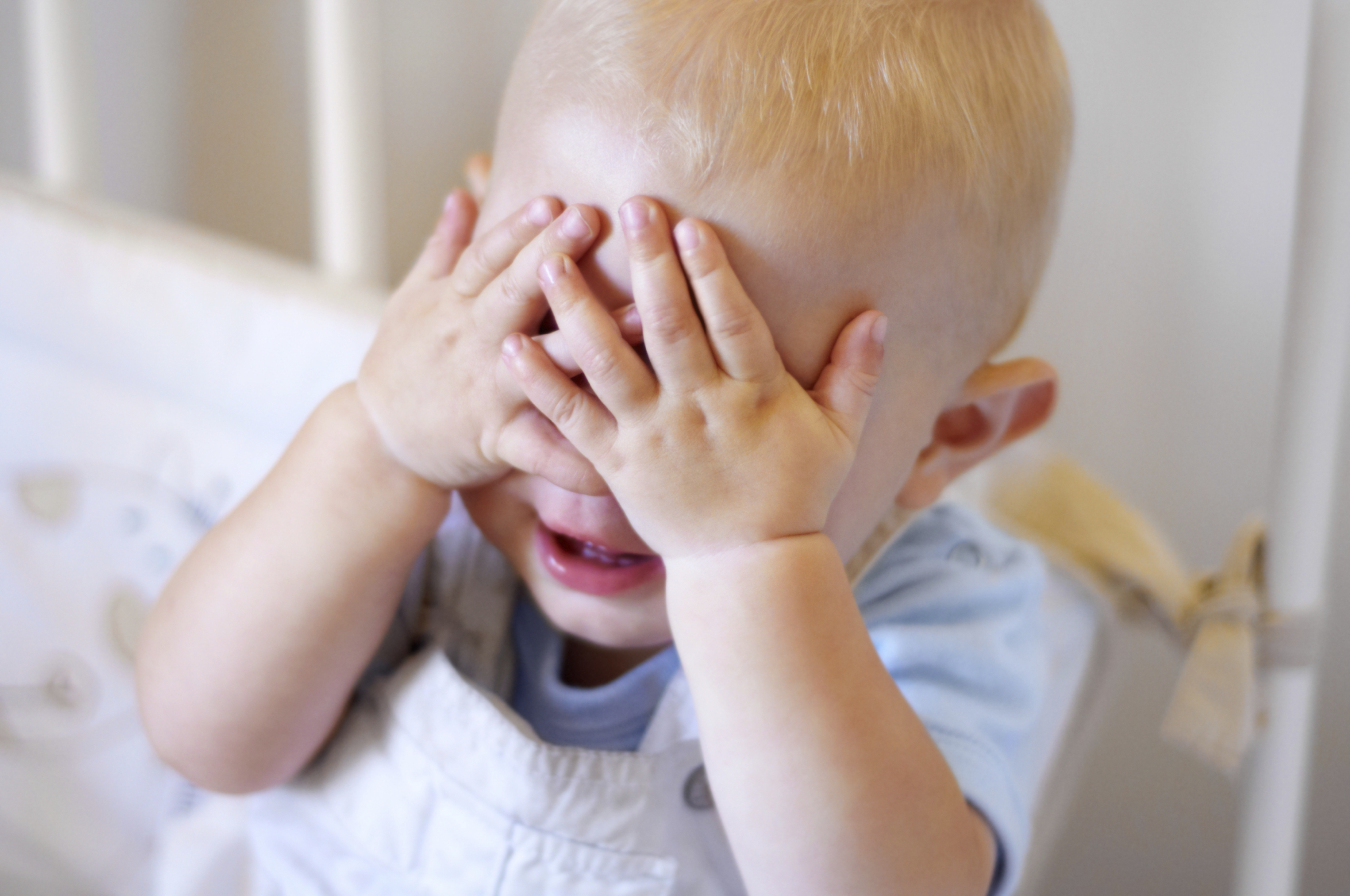 High angle view of a baby boy playfully covering his eyes at a Preschool & Daycare/Childcare Center serving Apex & Fuquay-Varina, NC