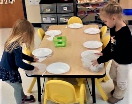 Young little preschool girls on discovering roles, preparing plates on the table at a Preschool & Daycare/Childcare Center serving Apex & Fuquay-Varina, NC