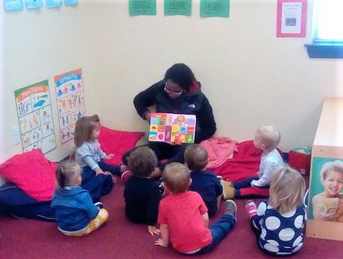 Teacher showing colorful pages of story book to group of toddlers